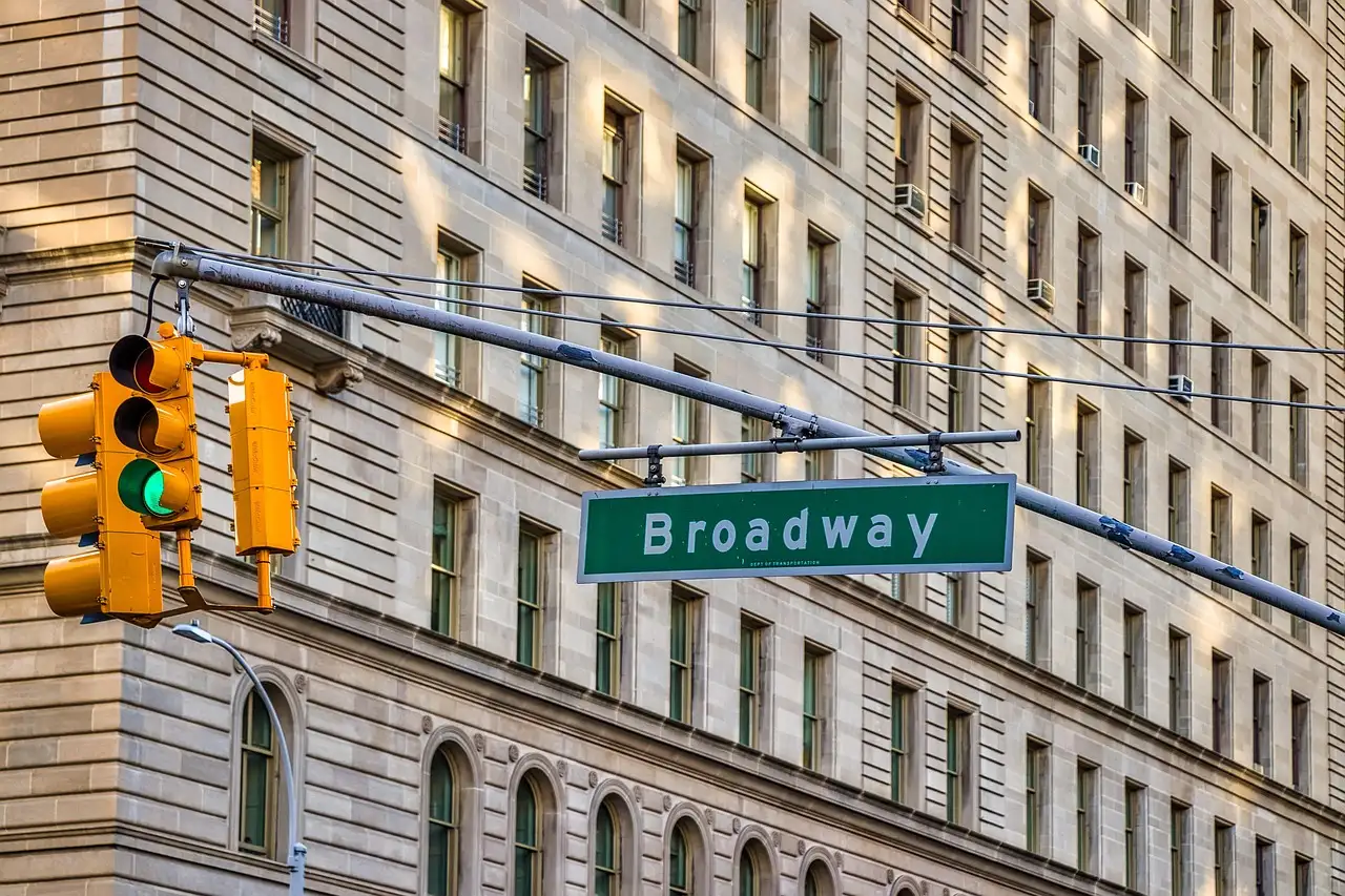 A green Broadway street sign and traffic light on a Manhattan corner