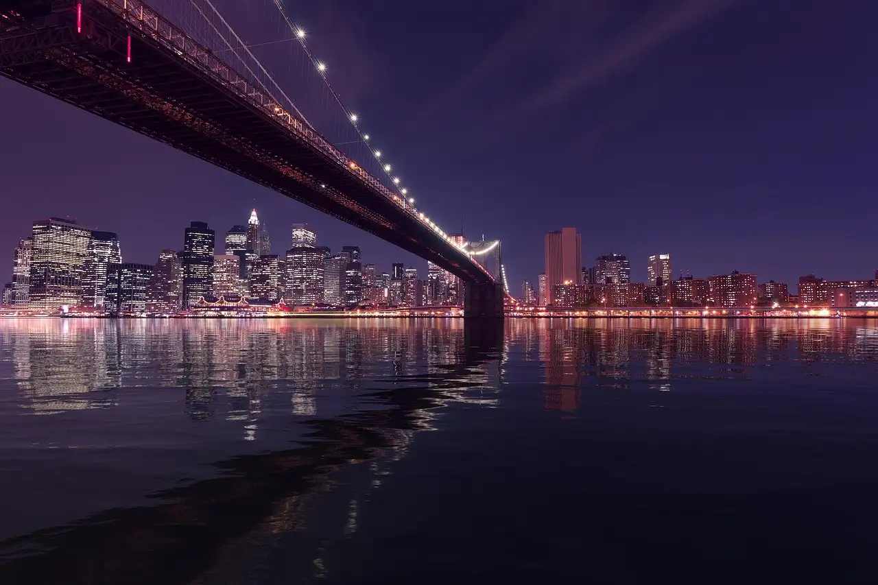 The Brooklyn Bridge at night, reflected in the river