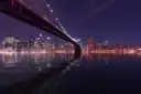 The Brooklyn Bridge at night, reflected in the river