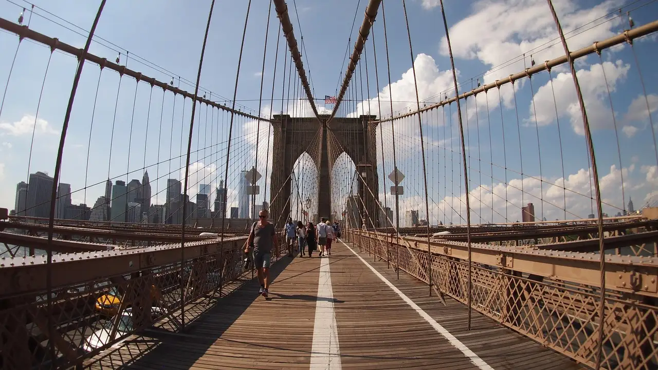 Walkers on the wooden promenade of the Brooklyn Bridge, heading toward the stone tower