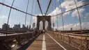 Walkers on the wooden promenade of the Brooklyn Bridge, heading toward the stone tower