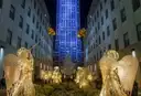 The Rockefeller Center Christmas tree at night, framed by lit angel figures and 30 Rockefeller Plaza