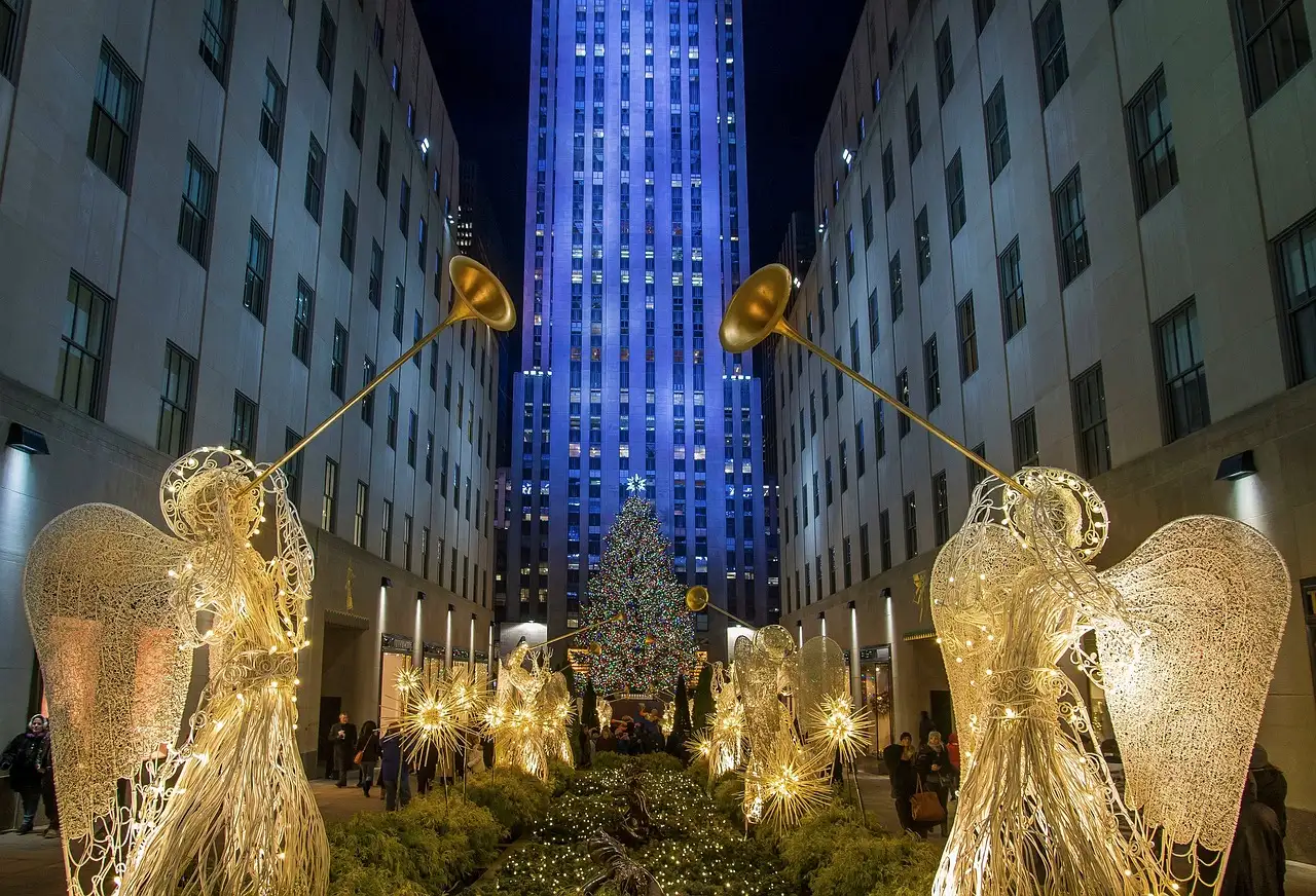 The Rockefeller Center Christmas tree at night, framed by lit angel figures and 30 Rockefeller Plaza