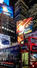 A red double-decker sightseeing bus in Times Square at night