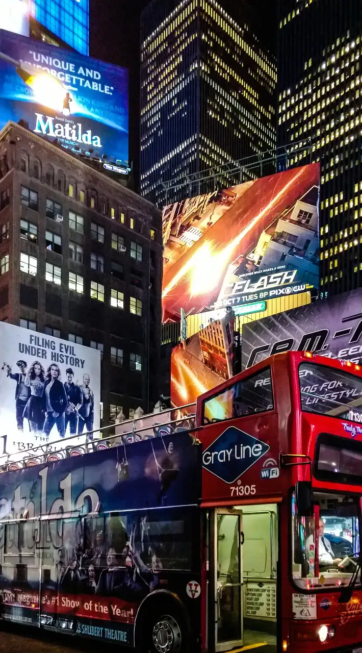 A red double-decker sightseeing bus in Times Square at night