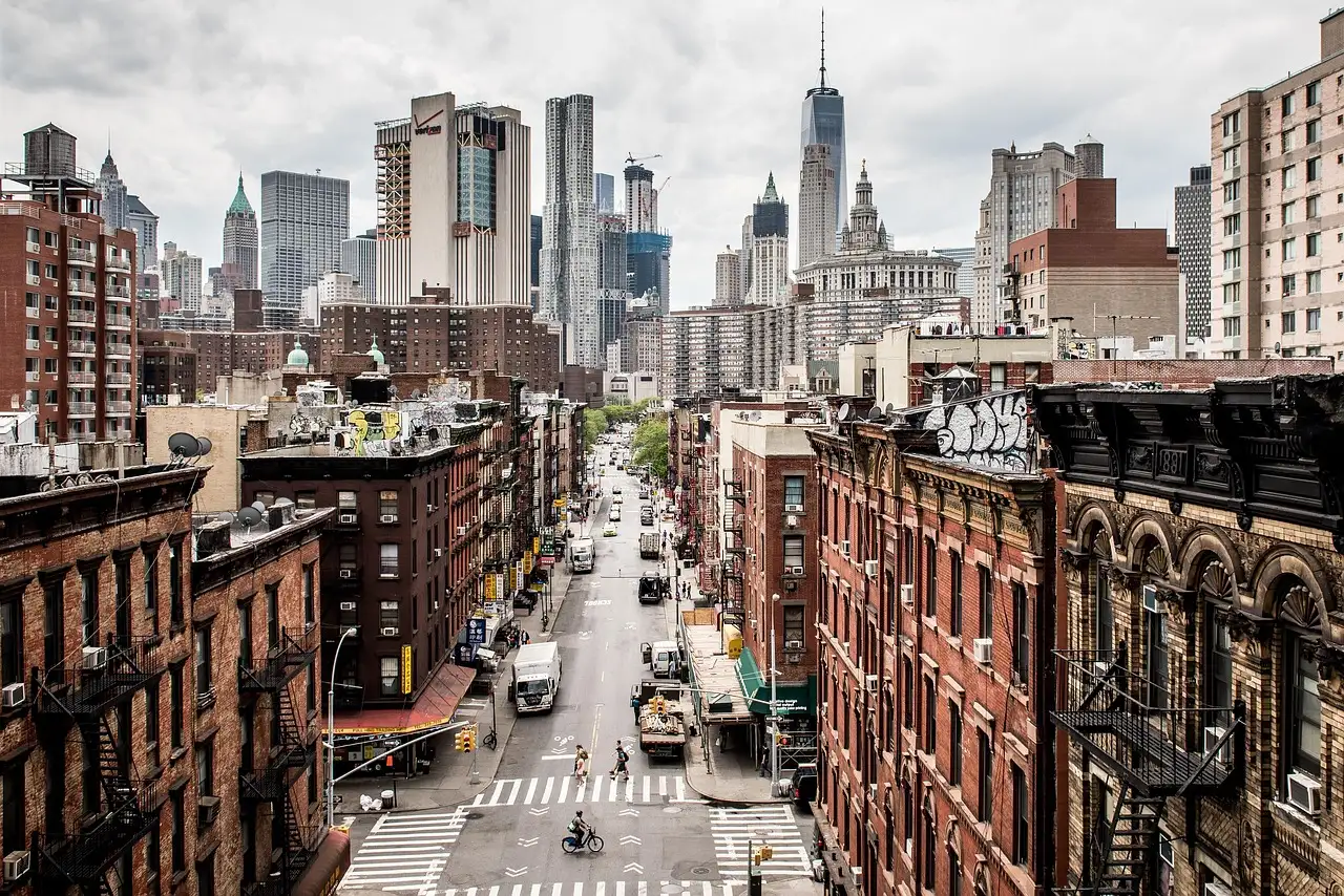 A downtown Manhattan street of brick tenements seen from above, with Lower Manhattan towers behind