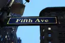 A Fifth Ave street sign against a stone building