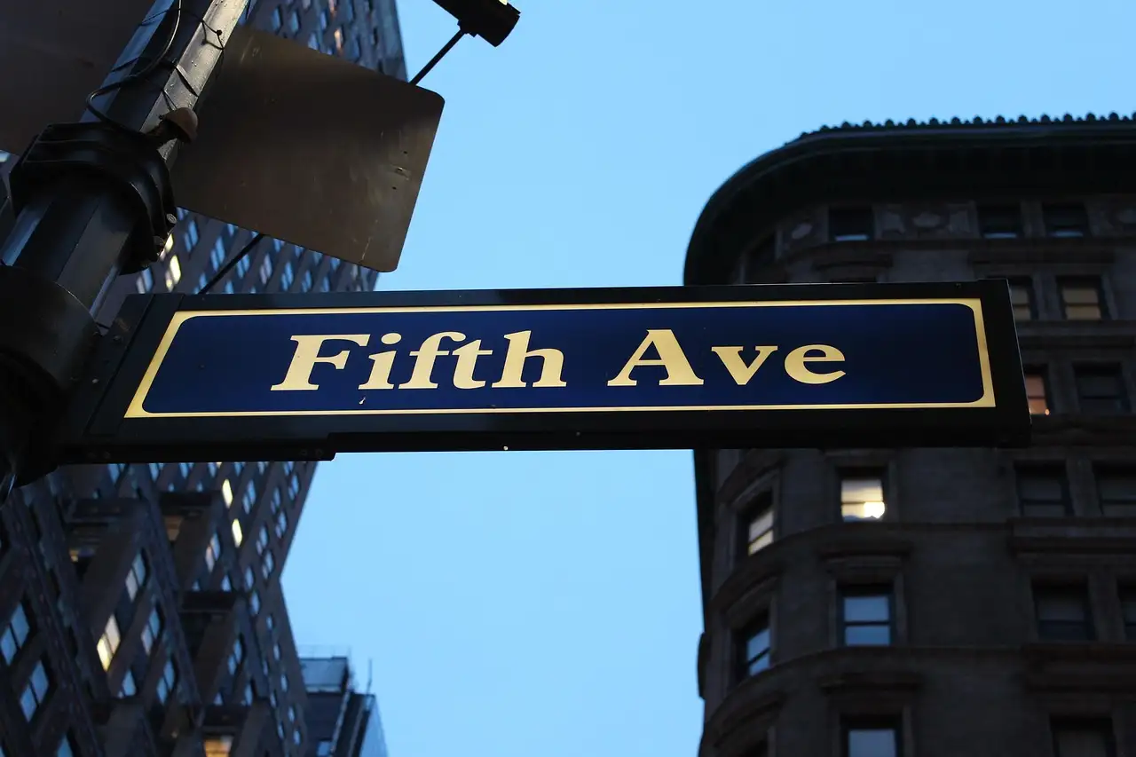 A Fifth Ave street sign against a stone building
