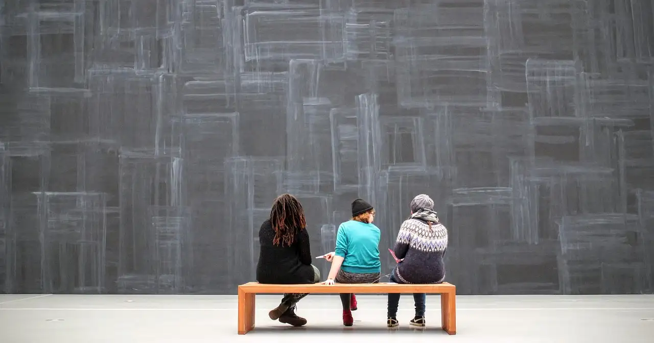 Visitors sitting on a gallery bench in front of paintings