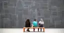 Visitors sitting on a gallery bench in front of paintings