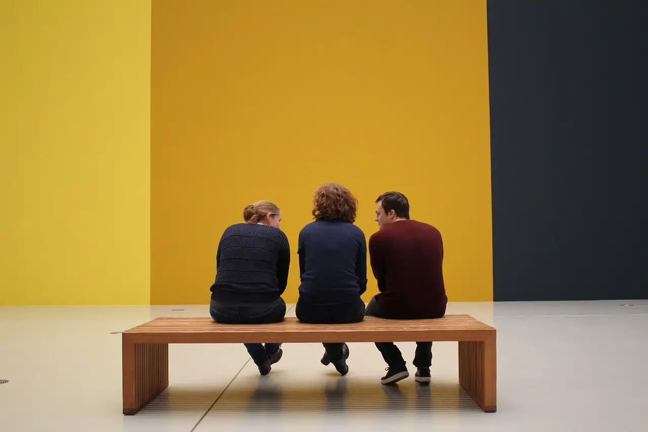 Visitors on a bench looking at paintings in an art gallery
