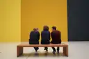 Visitors on a bench looking at paintings in an art gallery