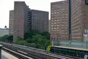 Harlem apartment towers and trees seen from an elevated subway platform