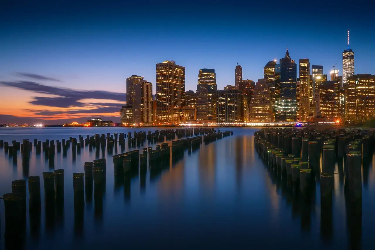 Lower Manhattan at dusk seen past old pier posts on the Brooklyn shore