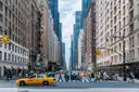 A Midtown avenue with a yellow taxi and people on the crosswalk