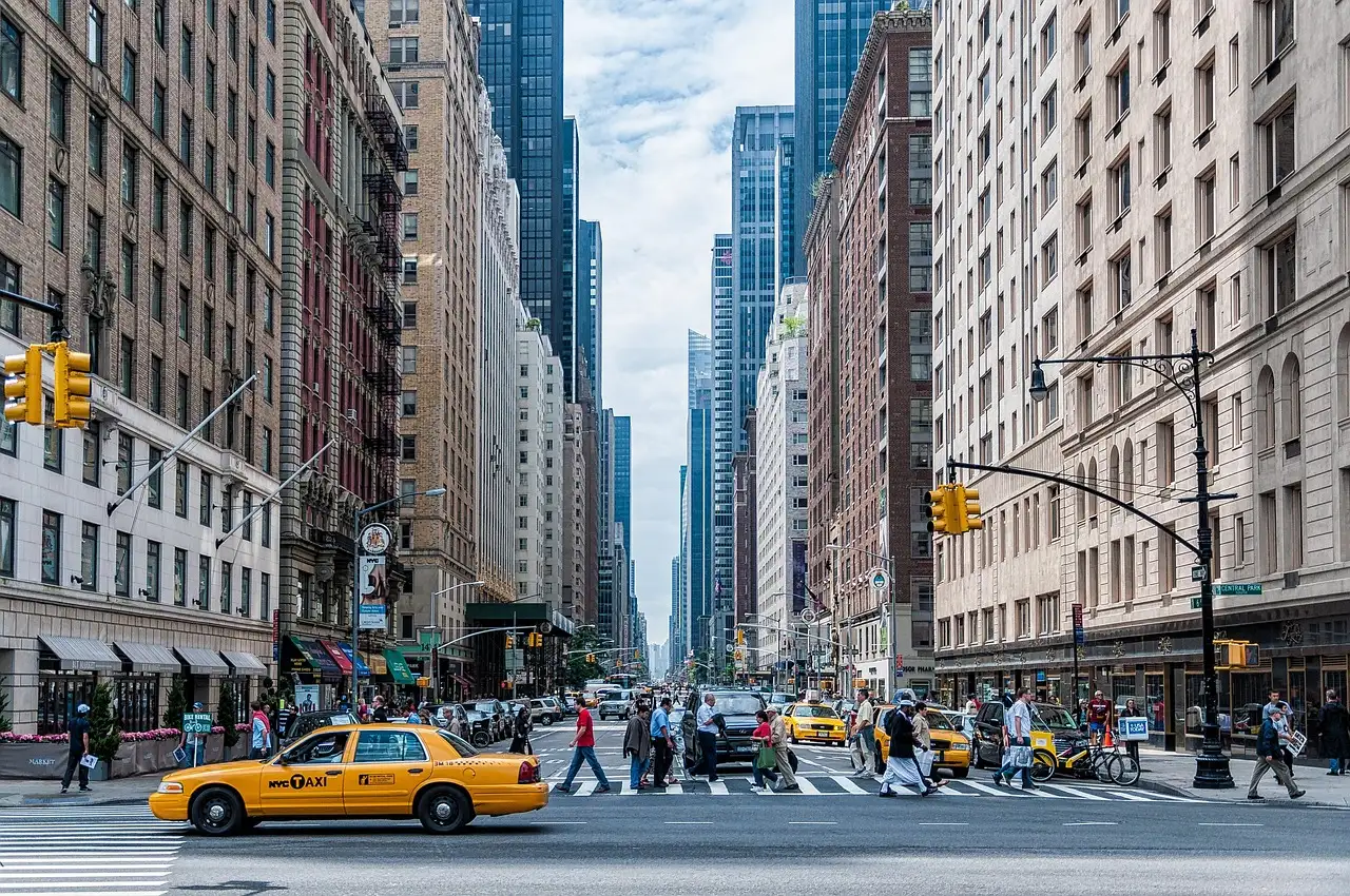 A Midtown avenue with a yellow taxi and people on the crosswalk