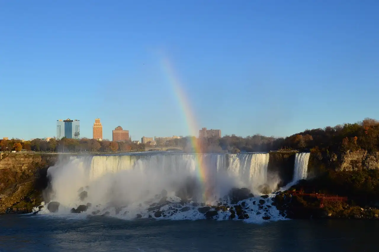 The American Falls at Niagara Falls with a rainbow in the spray and autumn trees on the bank