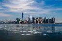 Lower Manhattan's skyline with One World Trade Center across the water on a clear winter day, with ice floating in front