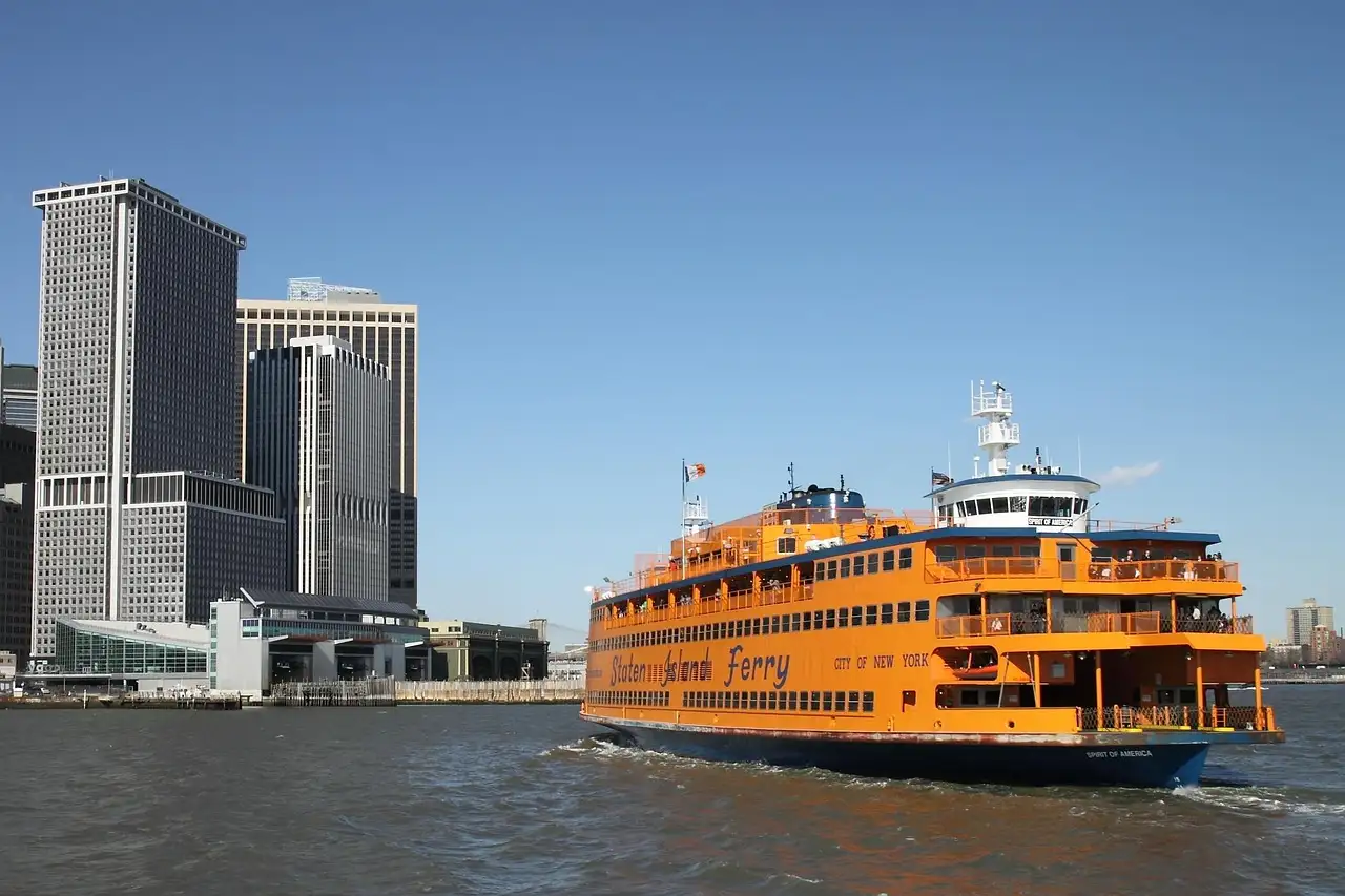 An orange Staten Island Ferry leaving Whitehall Terminal, with Lower Manhattan's towers behind it