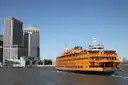An orange Staten Island Ferry leaving Whitehall Terminal, with Lower Manhattan's towers behind it