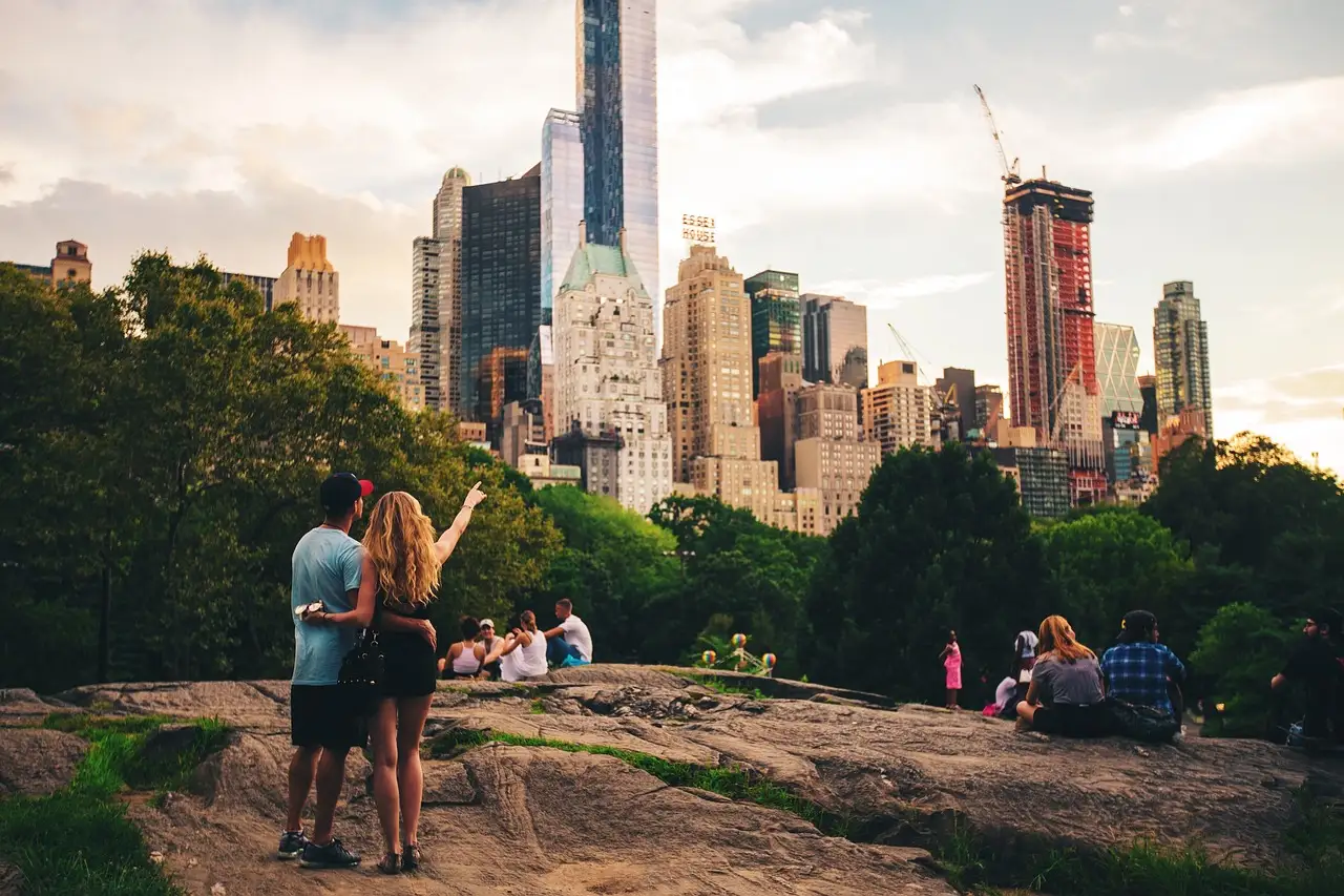 A couple standing on a rock in Central Park, looking at the Midtown skyline