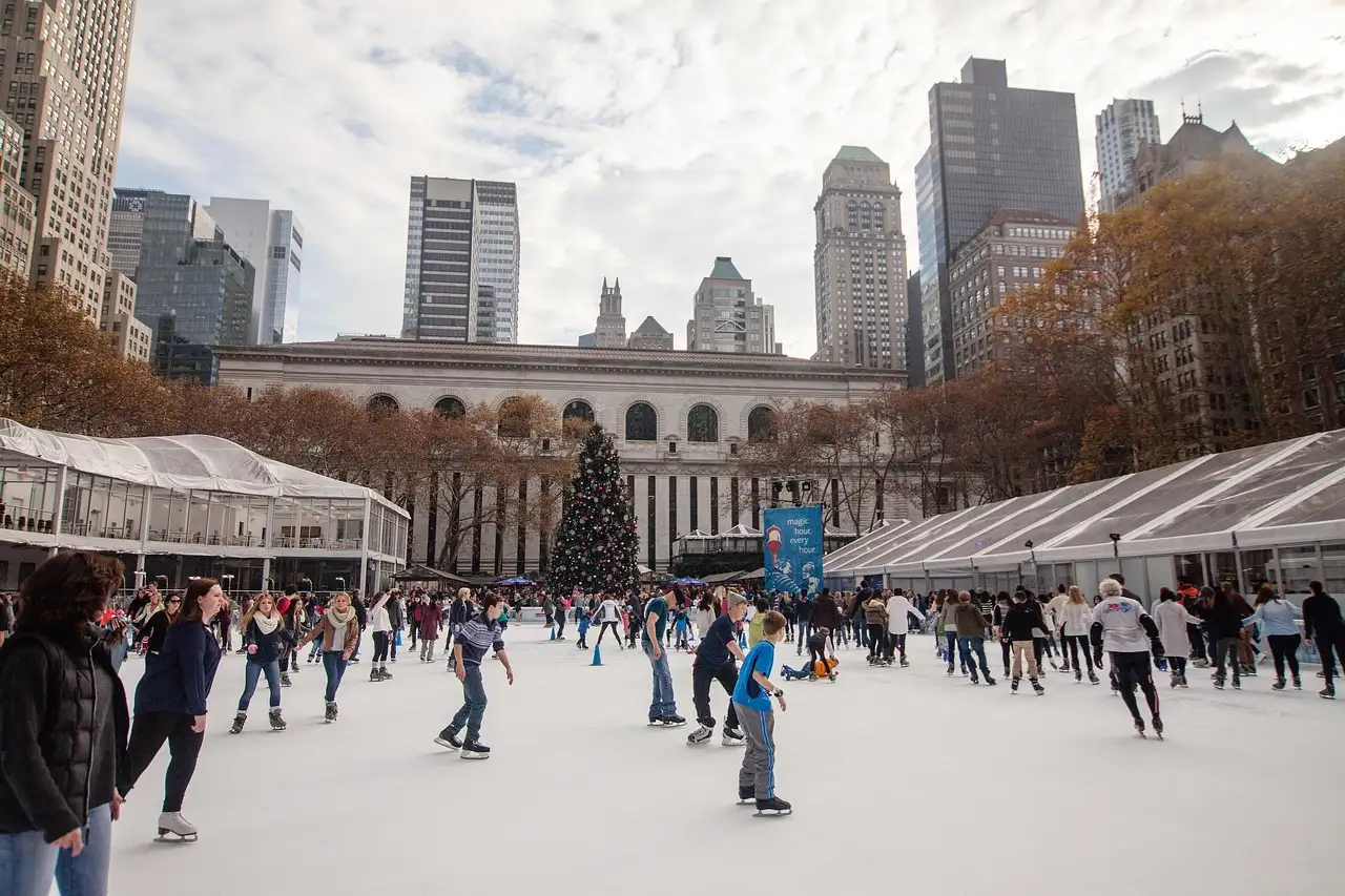 Ice skaters on the rink in Bryant Park with the holiday shops and a Christmas tree behind