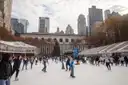 Ice skaters on the rink in Bryant Park with the holiday shops and a Christmas tree behind