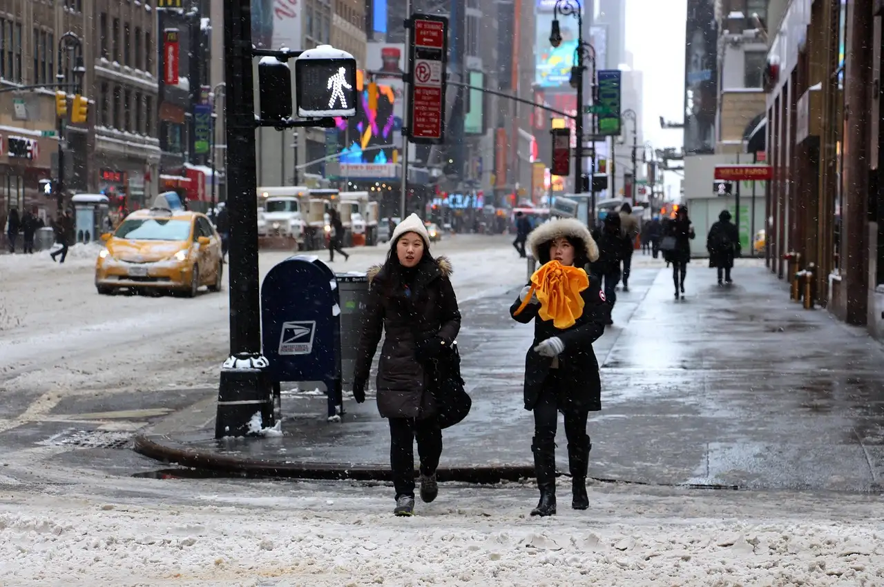People crossing a snowy street at Times Square with taxis behind