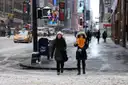 People crossing a snowy street at Times Square with taxis behind