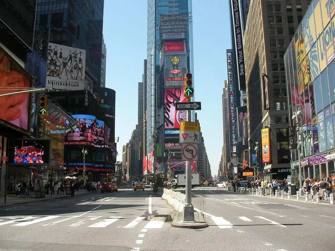 Times Square by day: a wide, quiet street between towers hung with billboards