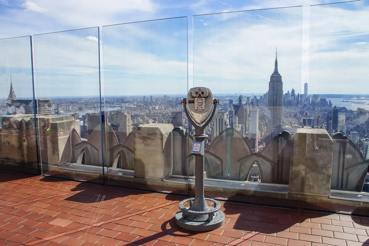 The Top of the Rock deck with a viewer, glass panels and the Empire State Building beyond