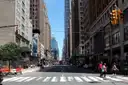 People walking over a wide striped crosswalk on a long, straight Manhattan avenue on a sunny day